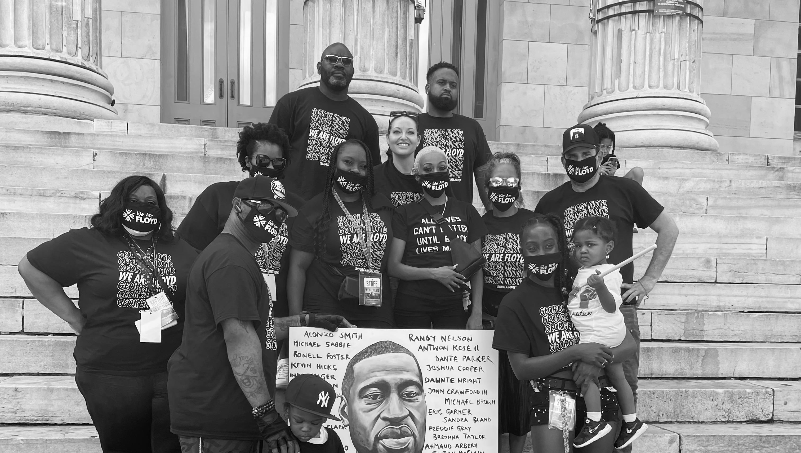 Black and White Group photo of the We Are Floyd and Confront Art members on the steps of a building with stone pillars. Artwork of George Floyd is held in the center of the photo.